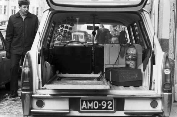 1970 n. . Liisankatu 9. Yksityisen sairaankuljetusyrityksen Peugeot-merkkinen ambulanssi, jonka takaluukku auki Liisankatu 9:n edustalla. Ihmisiä katsomassa ympärillä. Auton sisällä näkyy karu ja vähäinen välineistö.